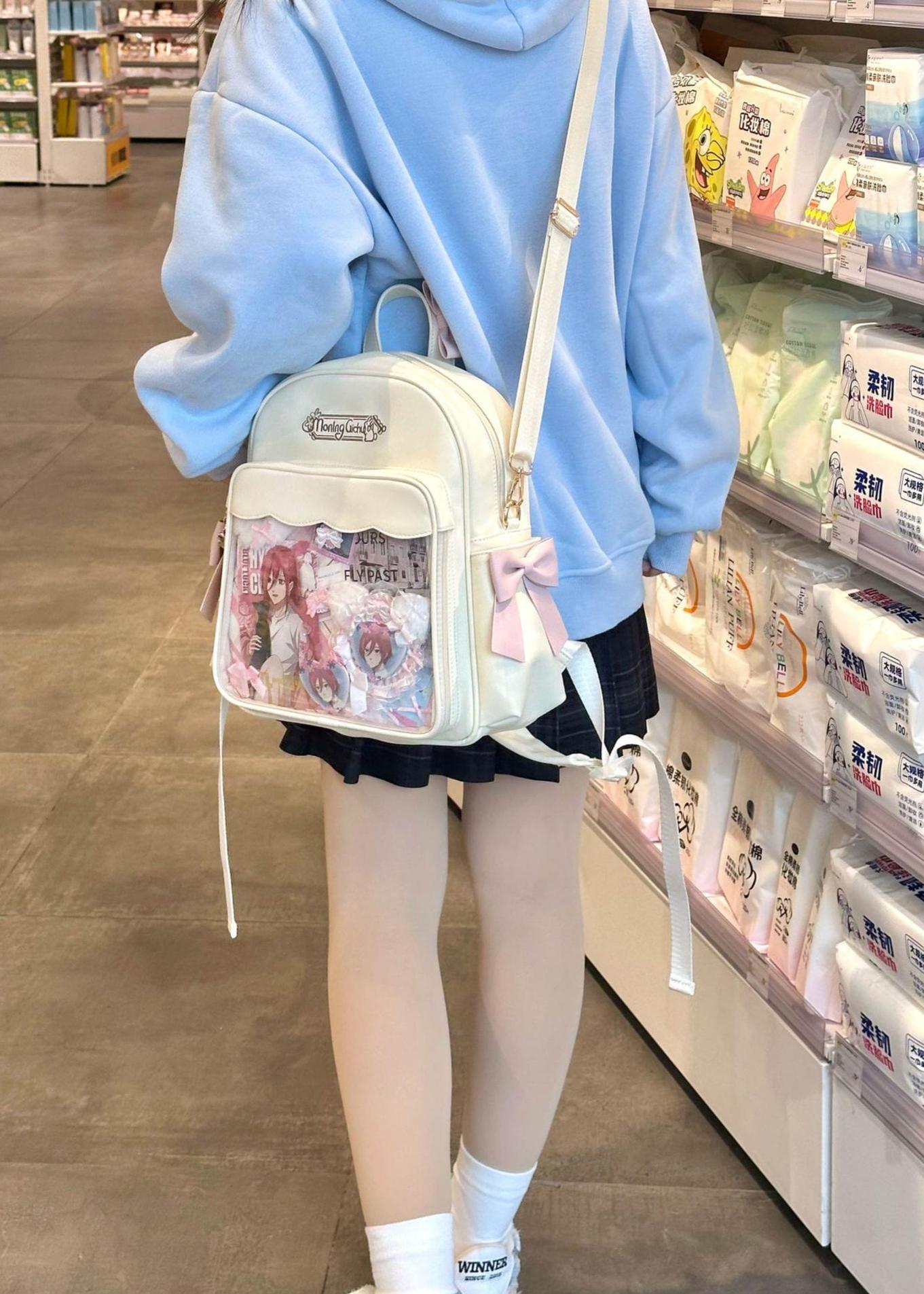 Jirai Kei transparent itabag backpack white with pink bow accents displayed in supermarket aisle showing anime merchandise showcase window