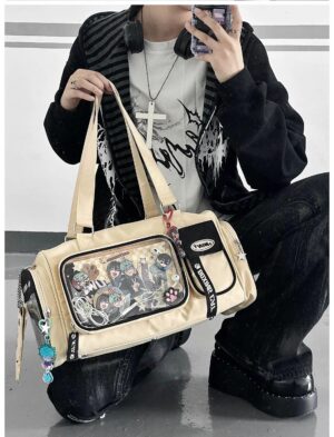 Khaki beige cylinder ita bag front view with dual top handles, anime print visible through transparent window, hanging character charms, worn with punk streetwear