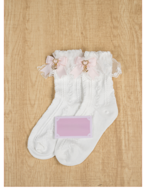 Light Pink Jirai Kei ankle socks with ruffled lace cuff and pink bow moon charm pendant, flat lay on wooden surface