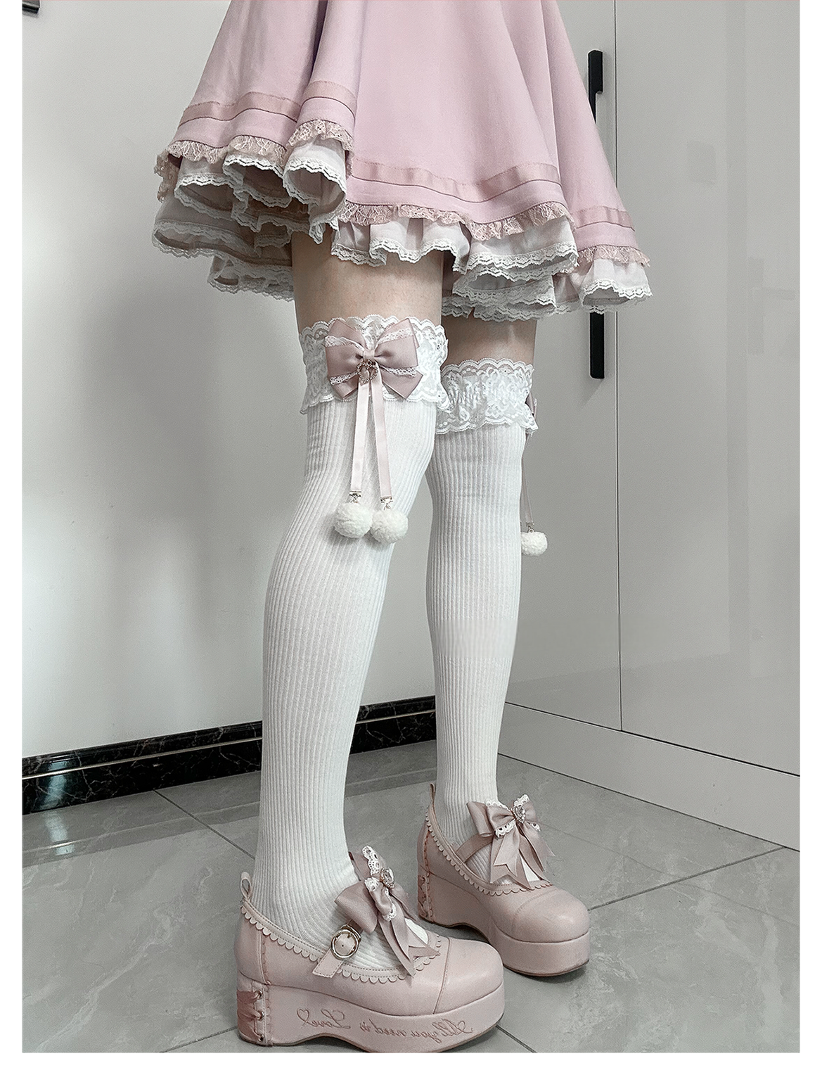 Jirai Kei mid-calf socks flat lay product shot showing pair with lace cuffs pink bows white pom-poms on neutral background highlighting design details