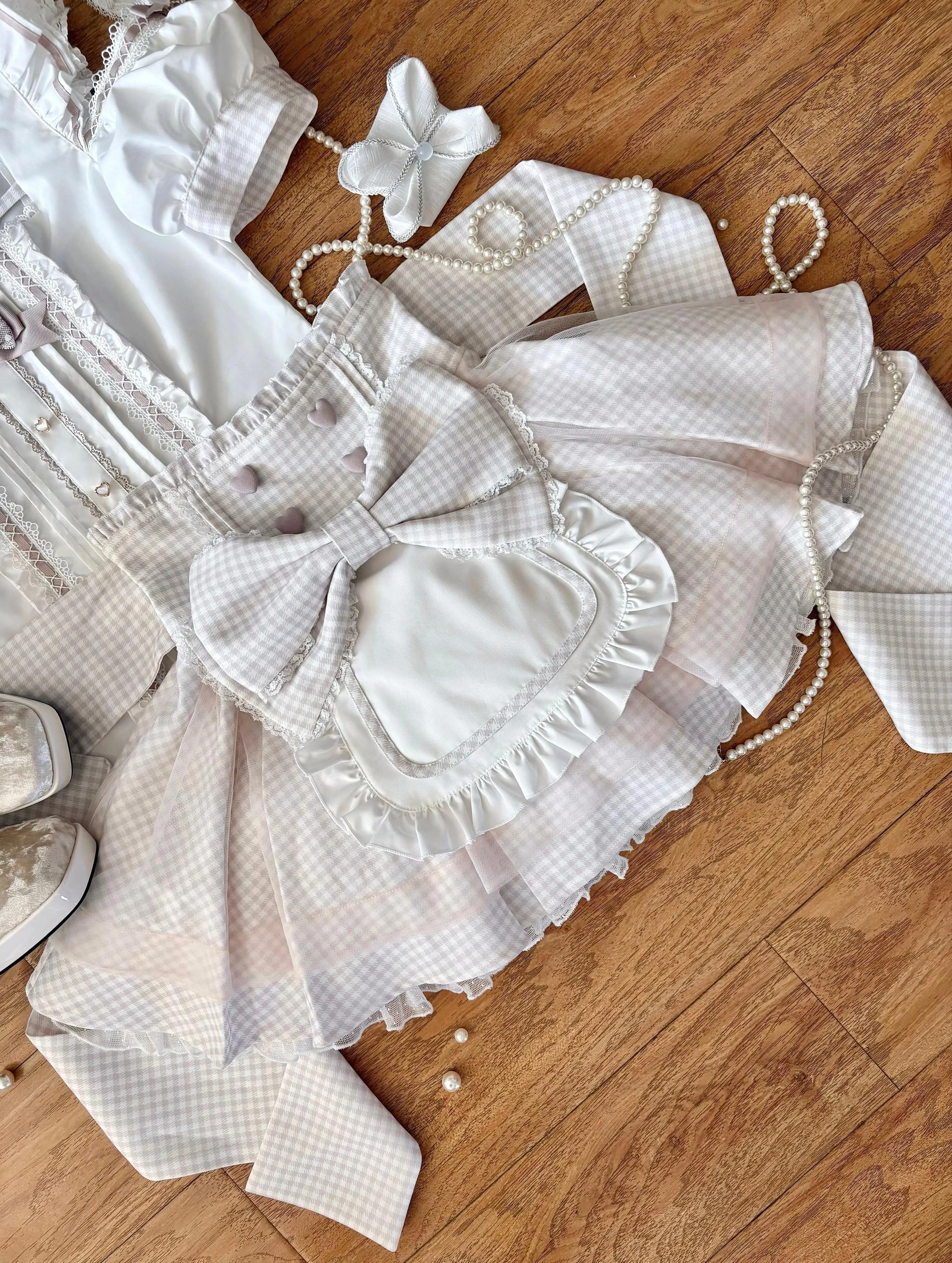 Flat lay top view of pink gingham Jirai Kei maid set showing ruffled lace apron details, heart-shaped bow closure, and overall construction on wooden surface