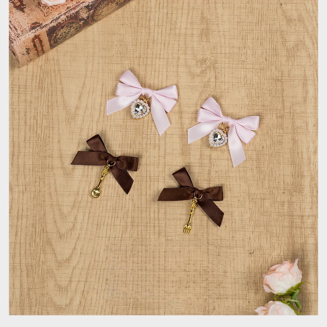 Pink and dark brown Jirai Kei cutlery pendant bow hair clips flatlay on wooden table with artificial roses and romantic aesthetic styling