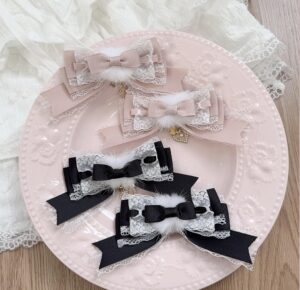 Black and white layered Jirai Kei bow hair clips with soft pom-pom and heart charm pendant, displayed on pink ceramic plate with lace cloth