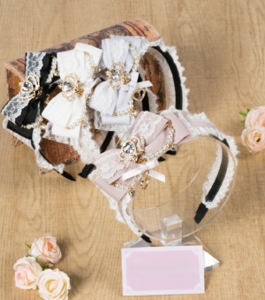 Assorted ryousangata bow lace headbands with rhinestone and pearl accents flat lay display showing multiple jirai kei color variants wooden desktop aesthetic artificial flowers styling