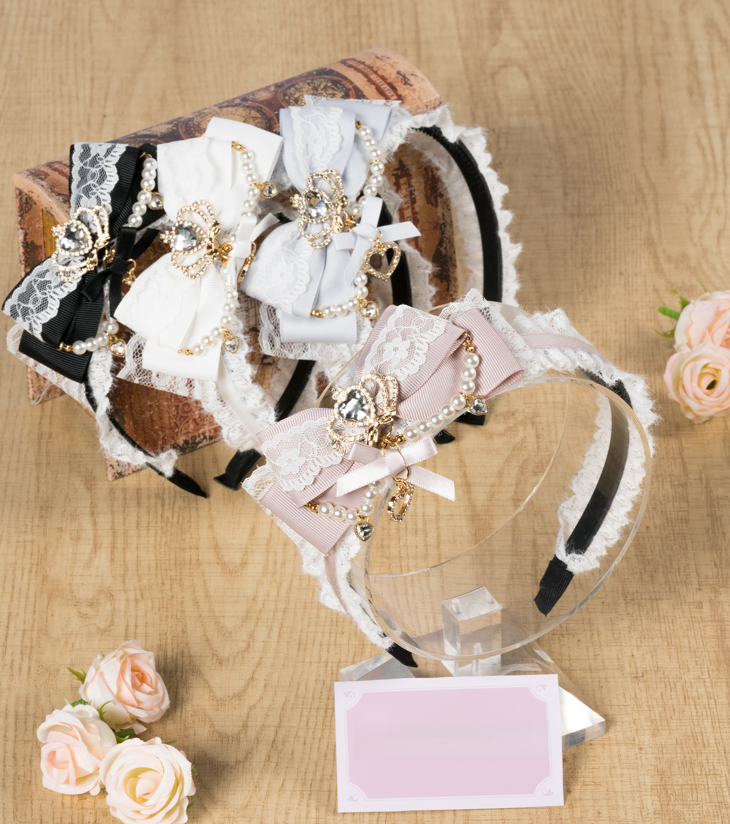 Assorted ryousangata bow lace headbands with rhinestone and pearl accents flat lay display showing multiple jirai kei color variants wooden desktop aesthetic artificial flowers styling