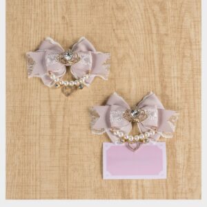 Dusty pink lace bow hair clips with crystalline rhinestone embellishment and pearl chain accent shown on wooden table with pink price tag