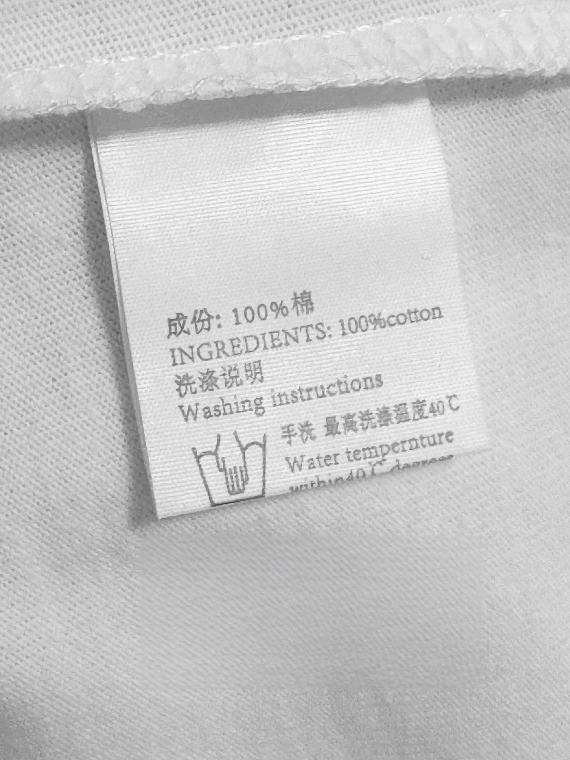 Clothing care label flat lay showing 100 percent cotton composition in Chinese and English, hand wash temperature instructions, off-white woven fabric care tag
