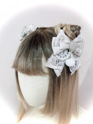 Gray-pink Ryousangata snowflake rhinestone ribbon bow hair clip with lace and pom-pom details, side rear view on mannequin with light brown bob hair
