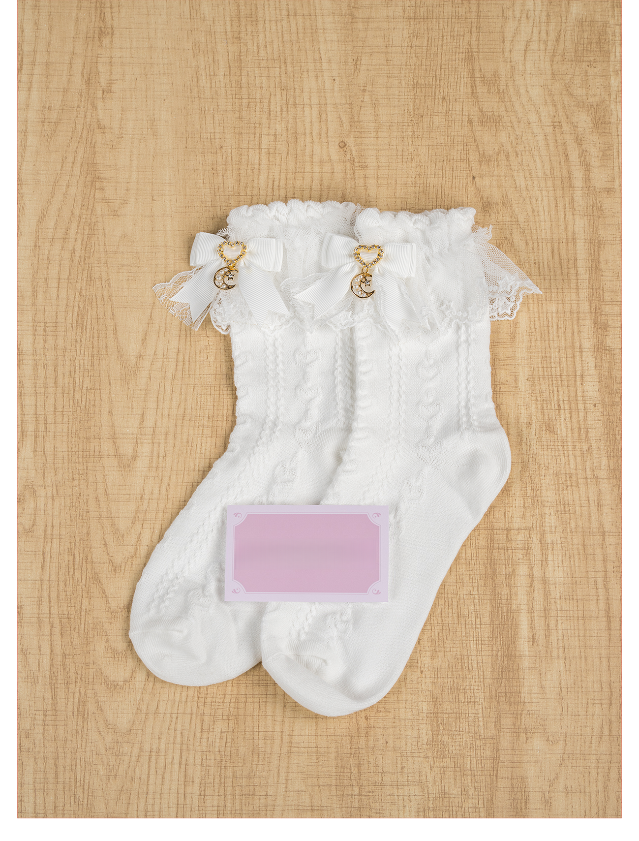 White Jirai Kei ankle socks with navy bow moon charm and ruffled lace cuff, worn with floral Lolita dress on tile floor front leg view