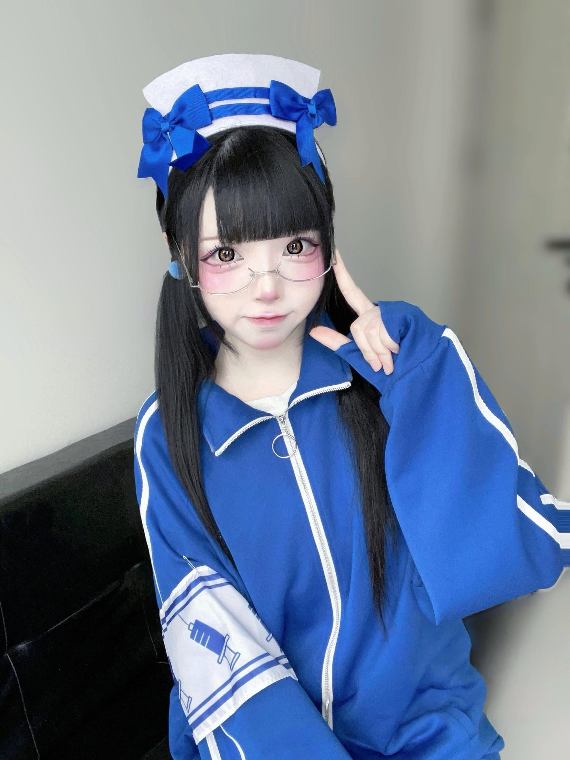 Close-up detail of blue track jacket with printed arm patch and nurse-style headwear indoor room setting