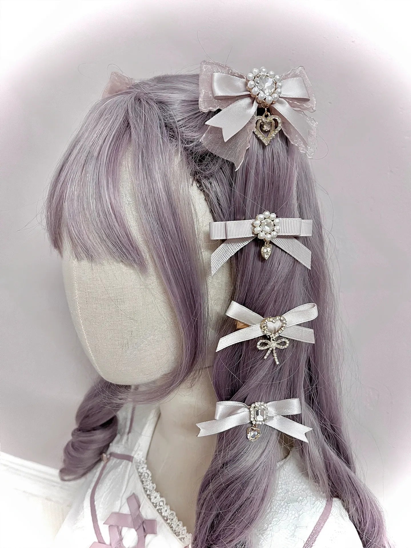 Beige cream colored bow hair clips with satin ribbon lace trim rhinestone and heart pendants on lavender mannequin head right rear view angle Jirai Kei fashion
