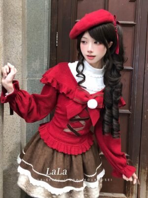 Red off-shoulder jirai kei sweater with dramatic flared sleeves and white fuzzy pom-pom details, paired with brown tiered ruffled skirt, worn by model against wooden doorway background