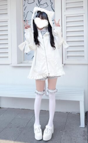 White cat-ear hooded Jirai Kei jacket full-body standing front view with ruffled hem lace-trimmed thigh-high socks outdoor bench setting