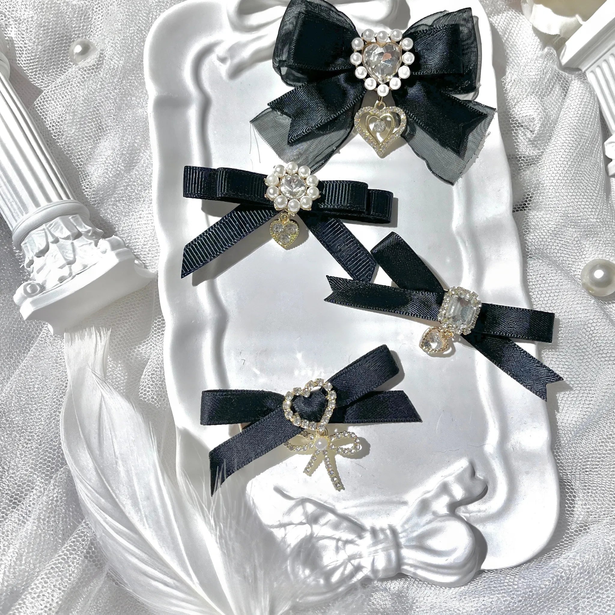 Black satin bow hair clips set with large rhinestone centers heart pendants displayed on decorative tray with lace background flat lay photography