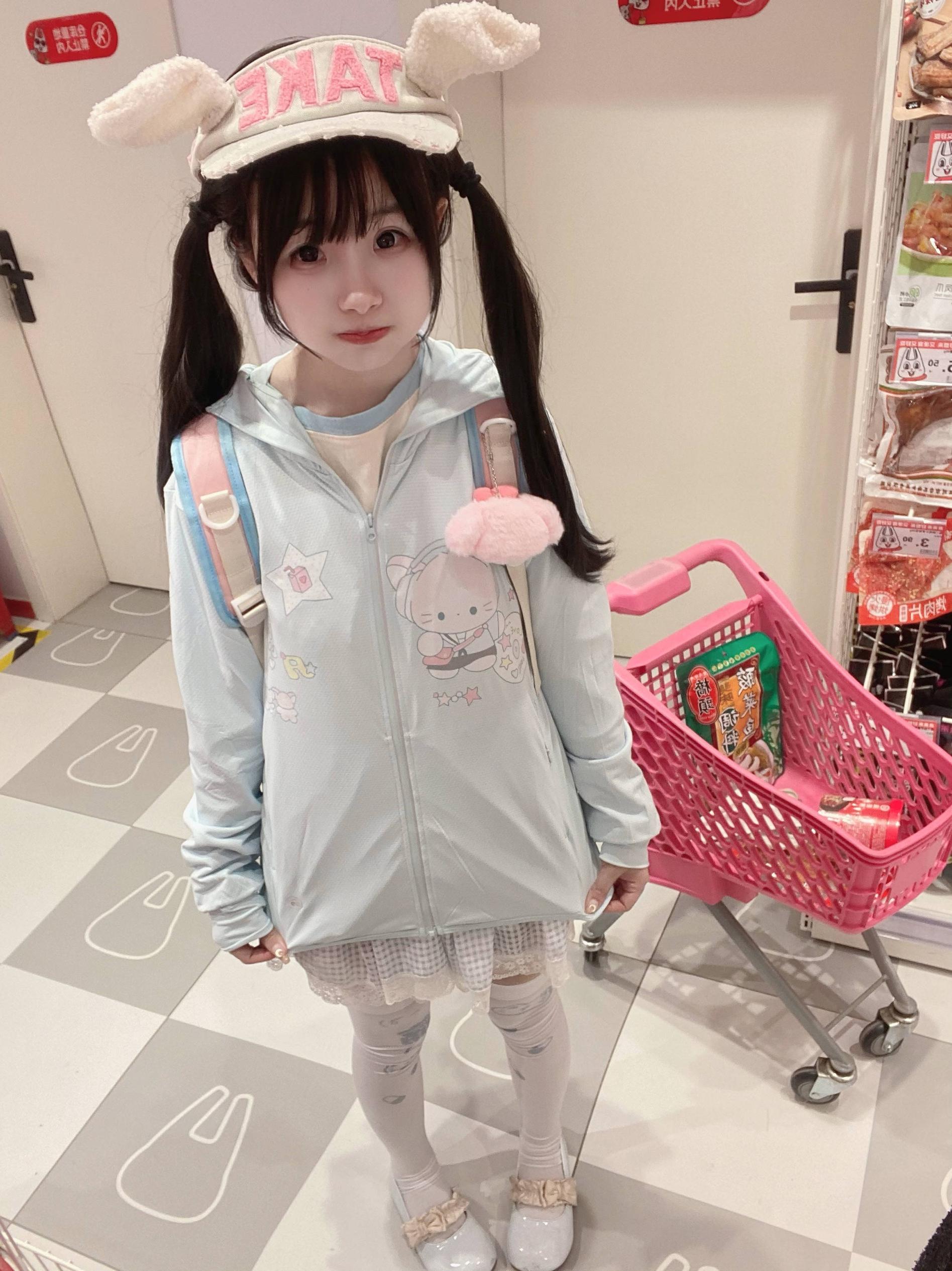 Full-body front view of water blue jirai kei sun-protective jacket on dark-haired twin-tail model with bunny ear accessories, convenience store setting