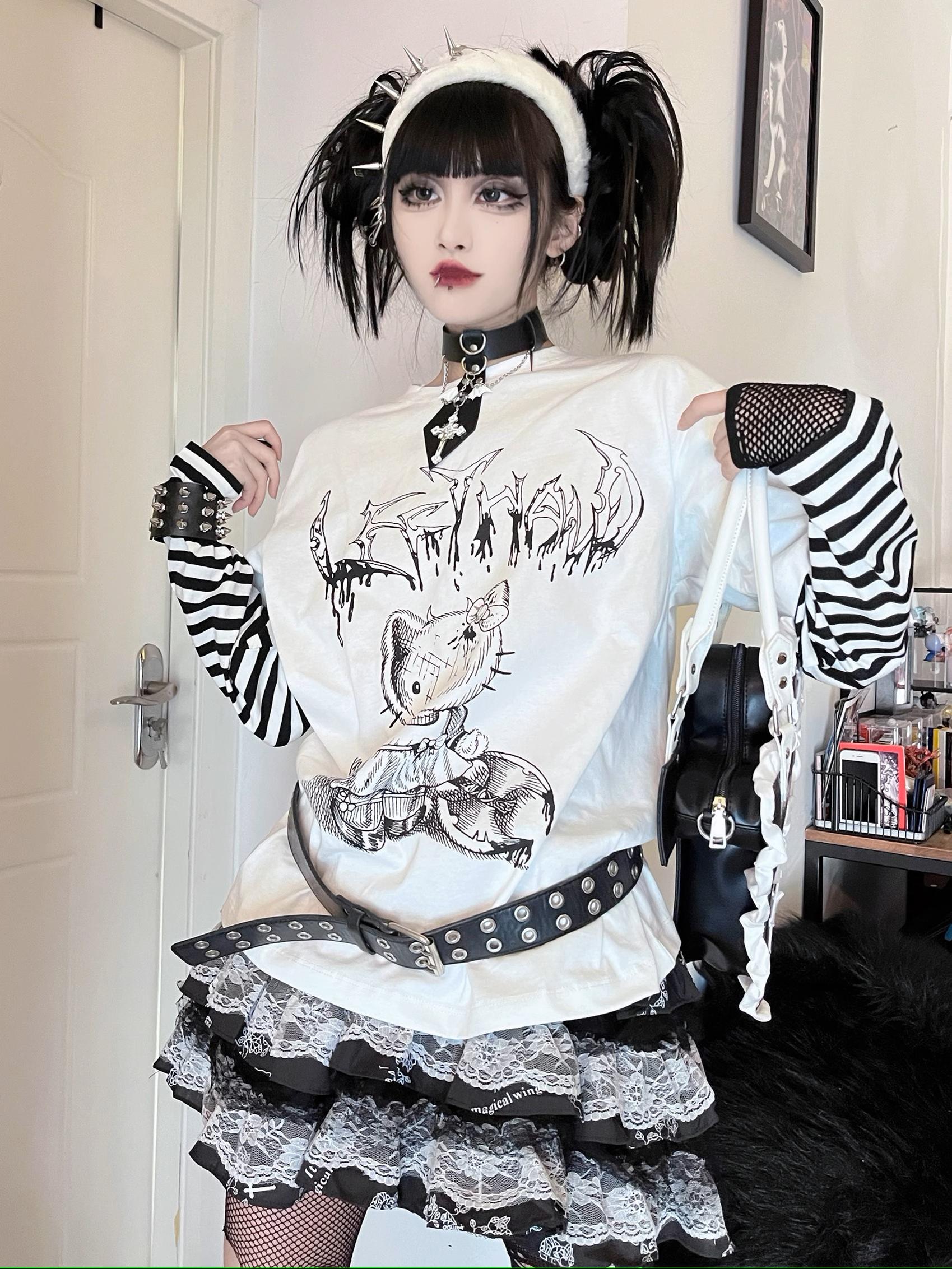 Full-body front view of black-white striped jirai kei fake two-piece long sleeve punk tee with cartoon cat graphic print, worn with studded belt and gothic twin-tail hairstyle