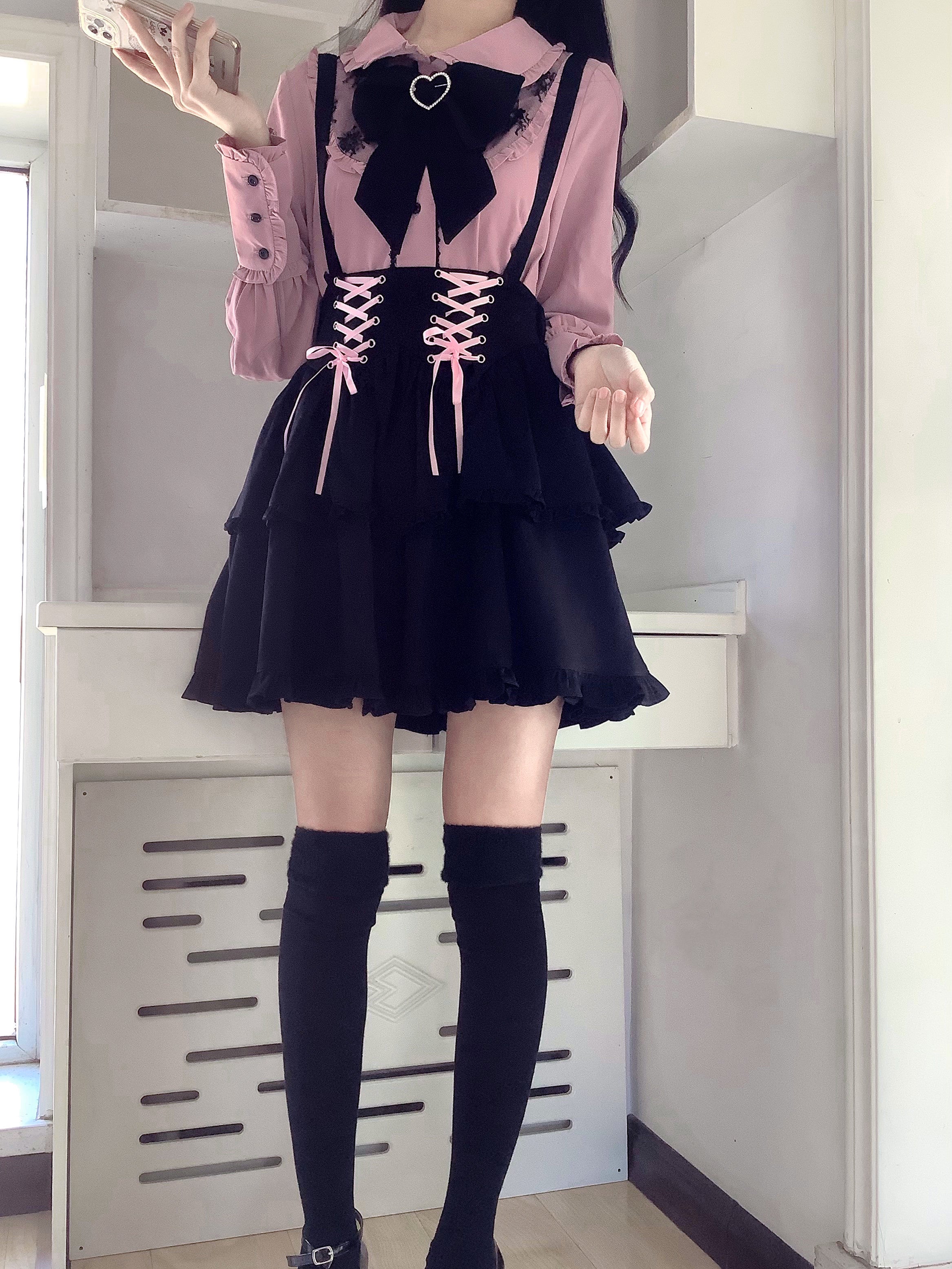 Front full-body Jirai Kei outfit photograph showing over-the-knee black socks, mini ruffled skirt with pink lace-up, shelf background, complete coordinate aesthetic