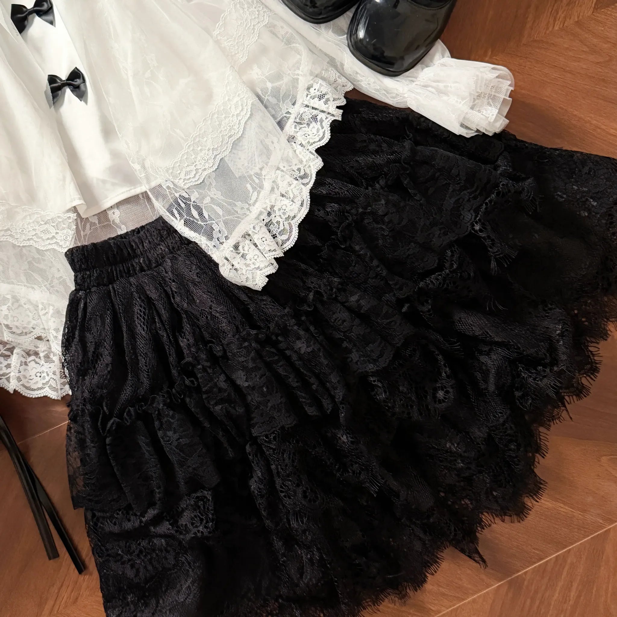 Black swan feather textured tulle Jirai Kei skirt with layered ruffles and lace trim hem displayed with matching off-shoulder blouse and black leather shoes, complete outfit styling