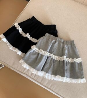 Top-down flat lay view of Jirai Kei layered cake skirts with white ruffled lace trim and detailed ruffle hems in black and gray colorways on wooden surface