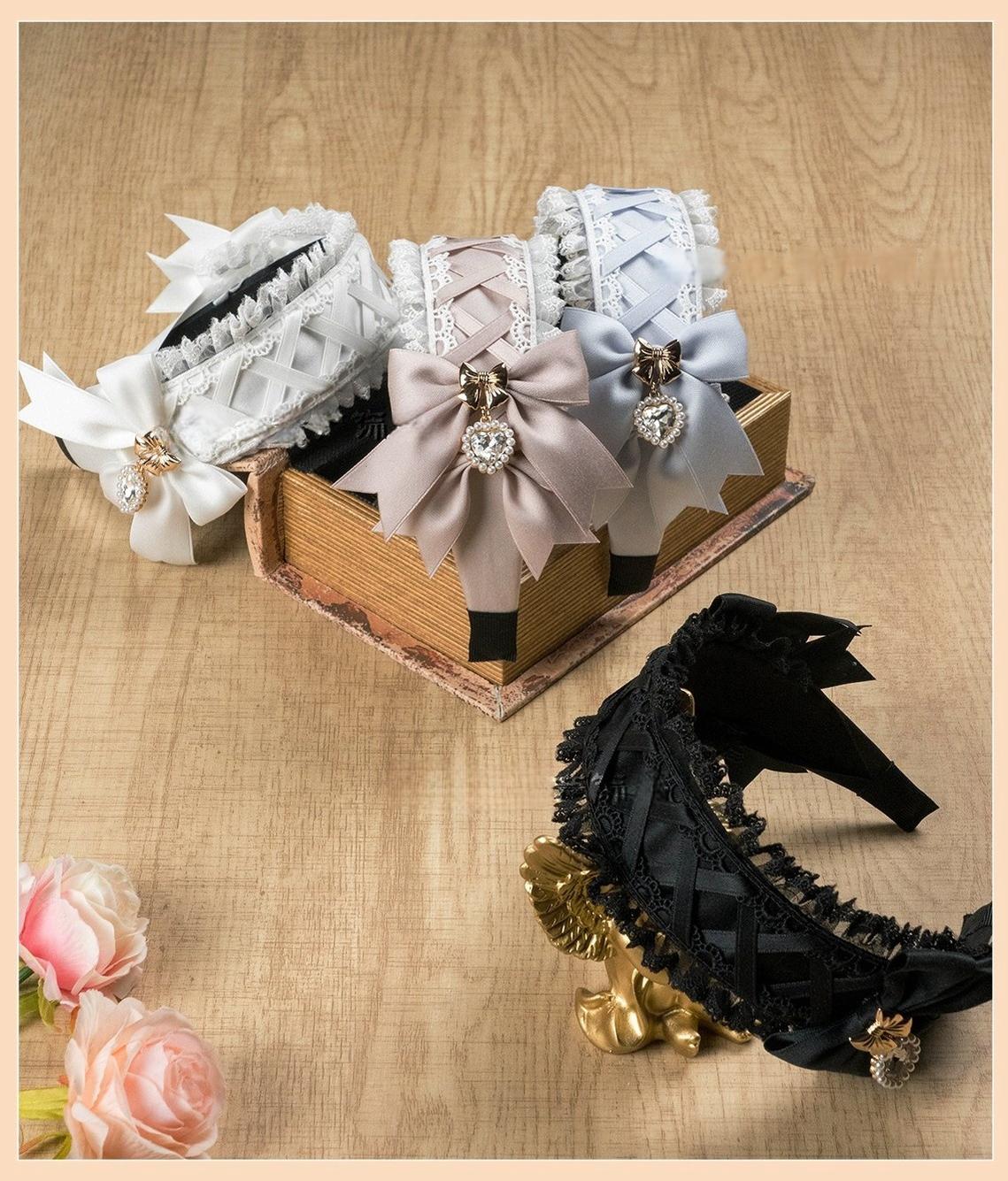 Angled top-down view of collection of Jirai Kei lace headbands on wooden table with decorative flowers and greenery, featuring satin bows, ruffled lace trim, and heart rhinestones in various color options