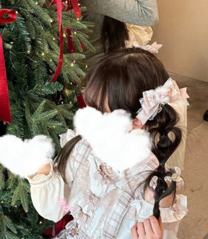 Girl wearing pink Jirai Kei bow hair clip with pom-pom in back view, styled with Christmas tree and Lolita outfit, lace trim and heart charm visible