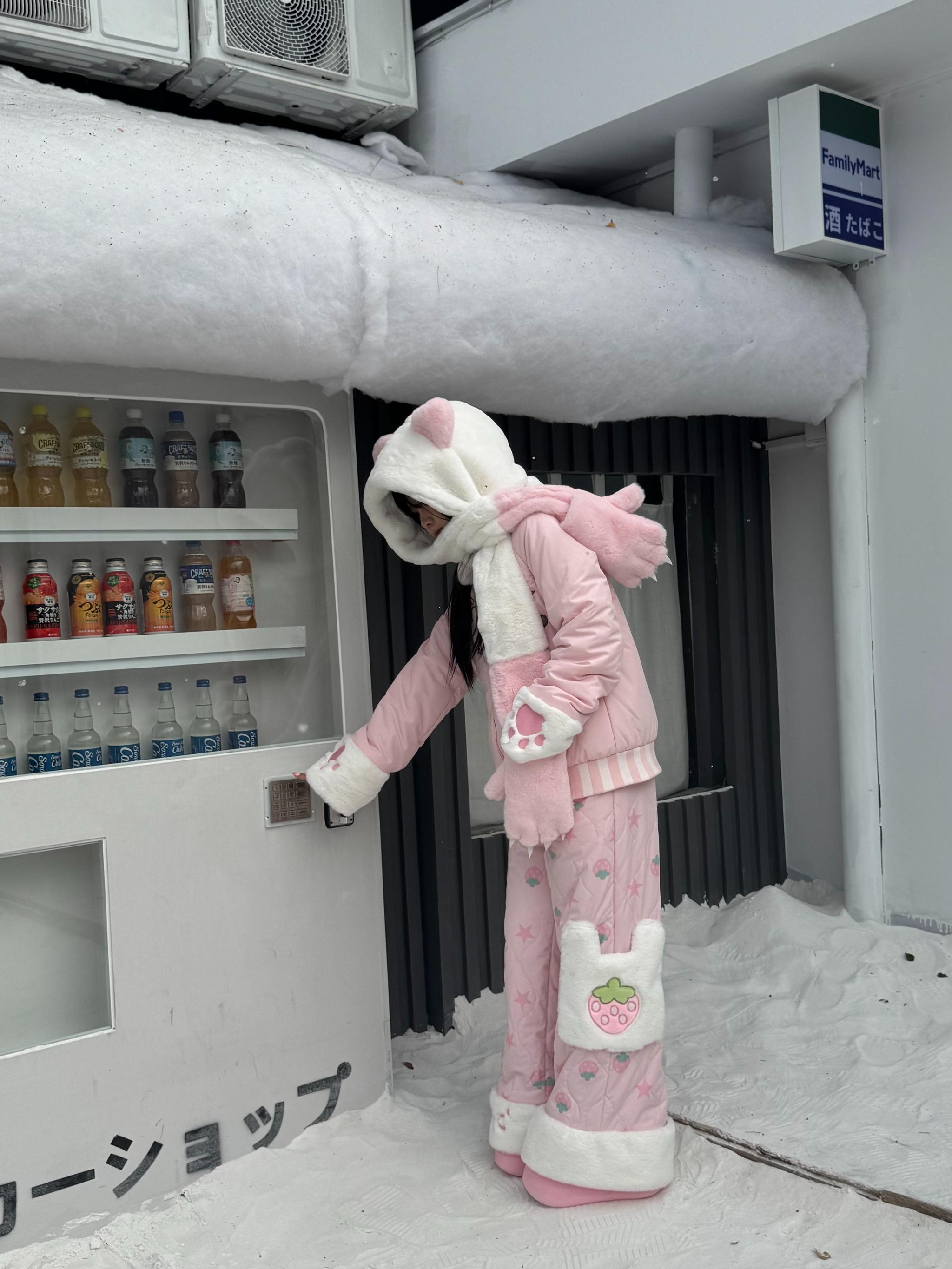 Pink Jirai Kei winter padded coat with hooded design, bear ear hood, fuzzy trim details, strawberry patch pants, side view of model at snowy vending machine