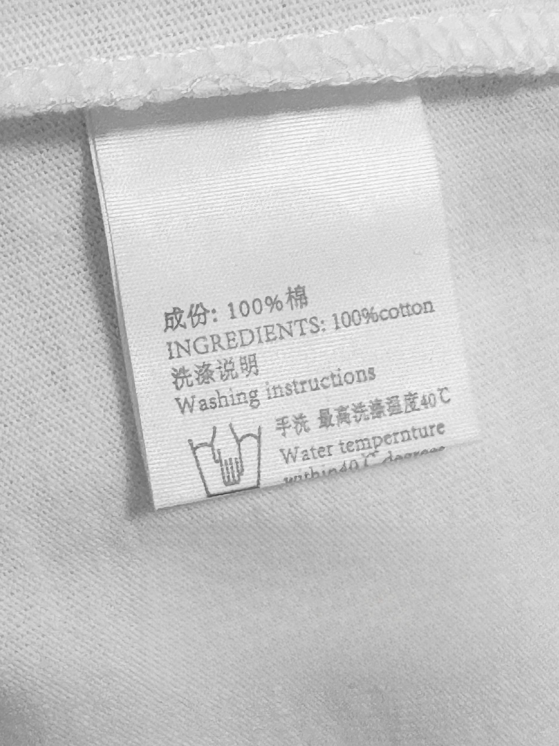 Close-up detail shot of bilingual care label on 100 percent cotton Jirai Kei t-shirt, showing washing instructions and fabric composition information