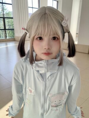 Front view of kawaii jirai kei water blue UV protection jacket with cute cat and star prints, modeled by blonde girl with twin-tails, indoor lobby setting with natural light