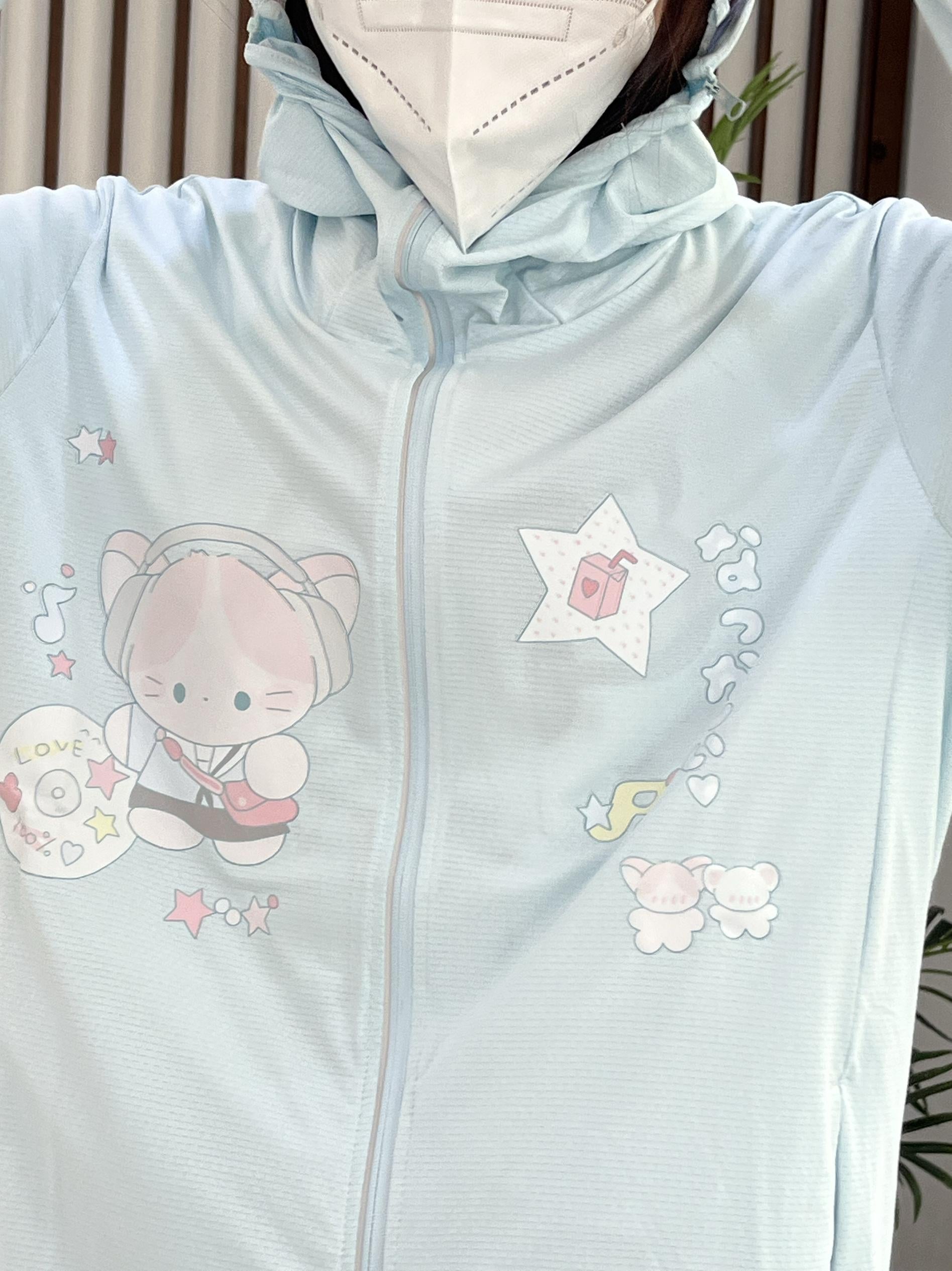 Flat lay close-up of jirai kei sun jacket front showing cartoon cat, star, and musical note embellishments, fine mesh protective fabric with face mask detail