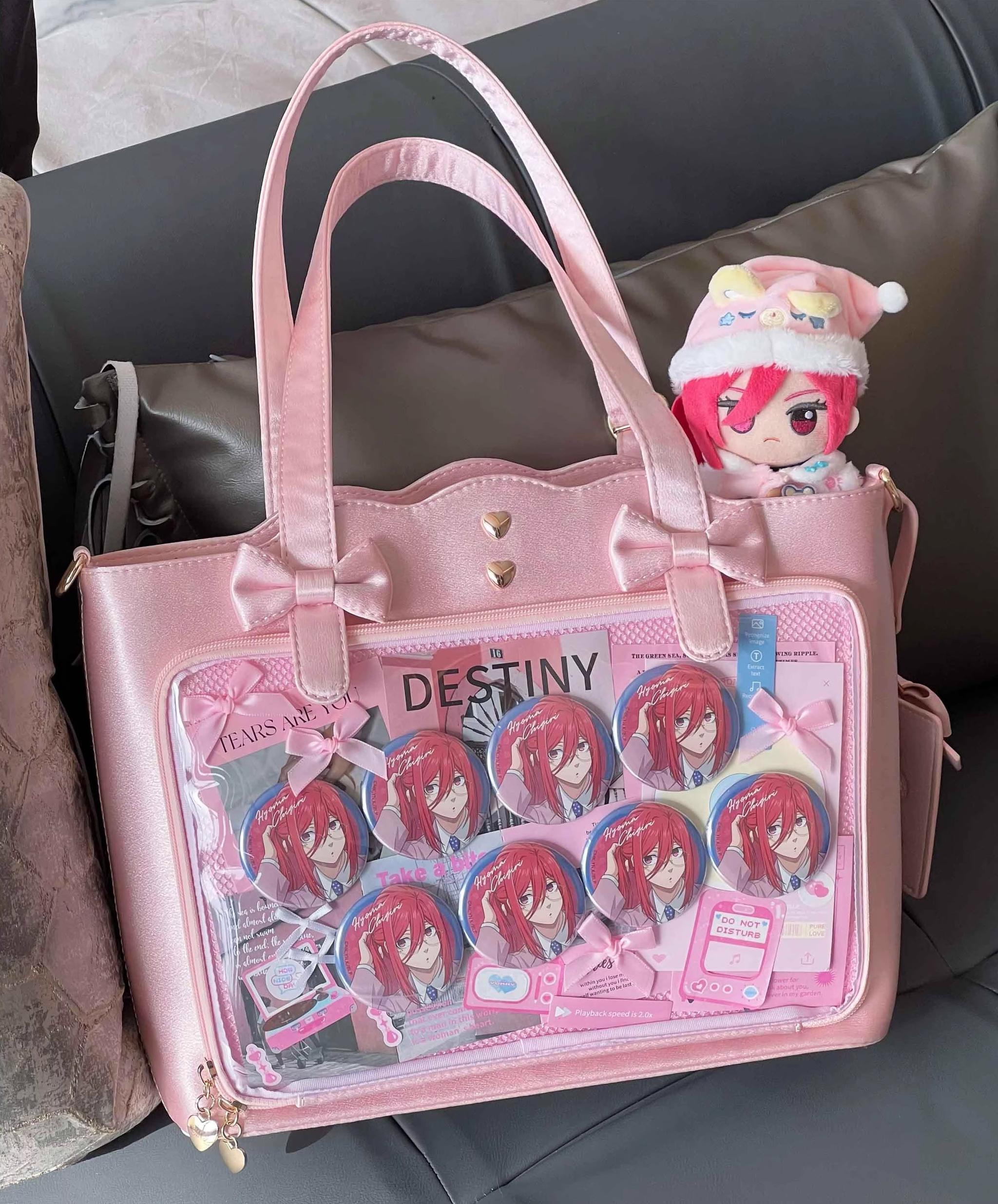Pink large Jirai Kei ita bag front flat display view positioned beside dark gray sofa, with adorable plush doll sitting on top, large clear anime pin window display, and heart-shaped metal studs