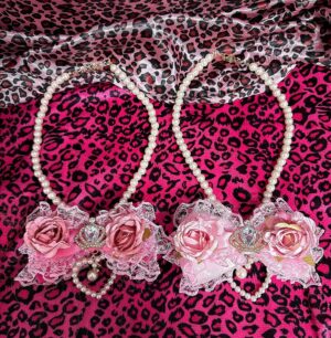 Jirai Kei pearl necklace with pink floral lace bow and rhinestone heart charms flat lay display on leopard print fabric