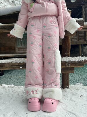 Full body front view of strawberry Jirai Kei quilted winter pants outfit worn with matching fuzzy-trimmed jacket and pink casual shoes in snowy outdoor area showing all-over fruit print and white ankle cuffs