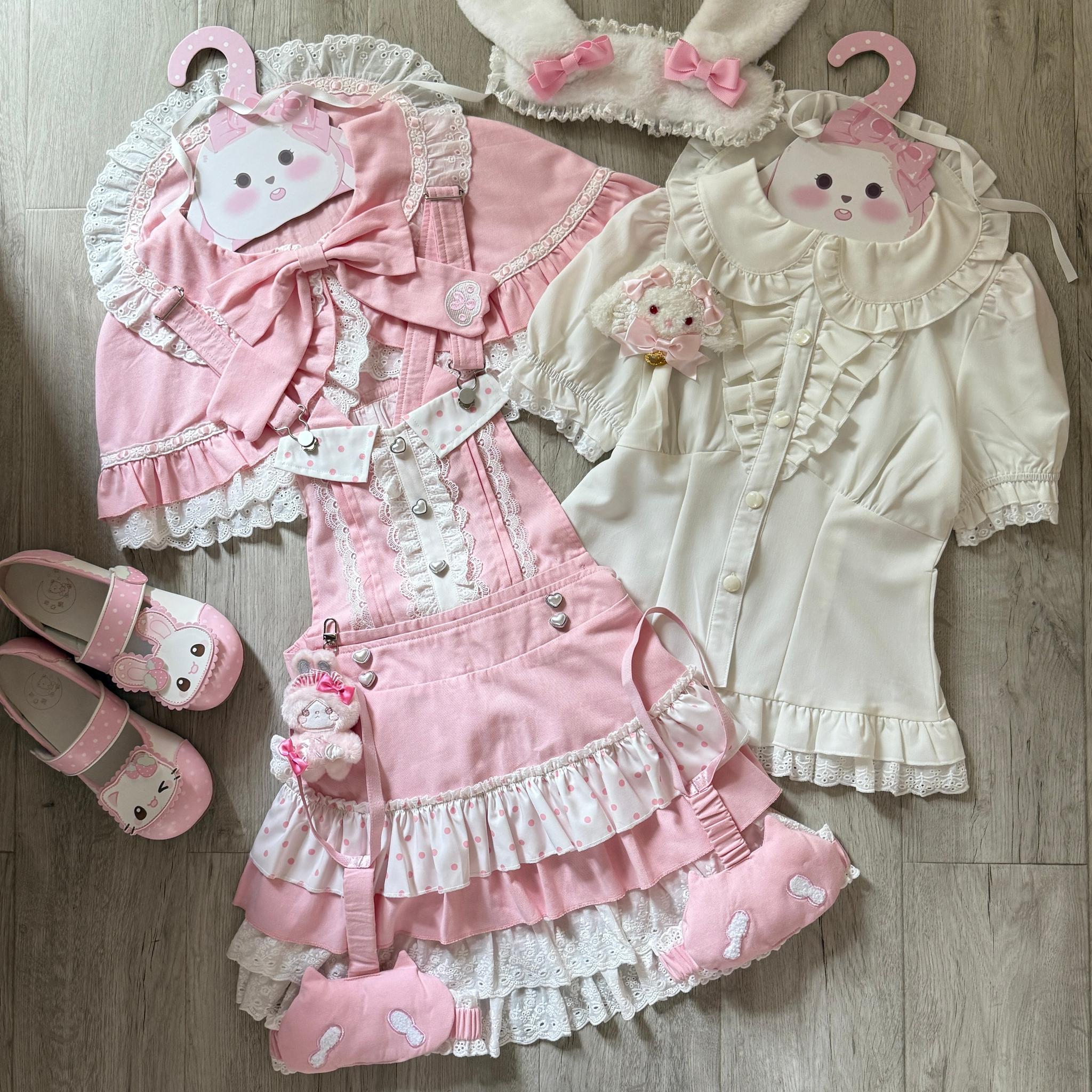 Complete kawaii jirai kei lolita outfit set flat lay display, suspender salopette dress with matching pink shoes, cat-themed decorations, ruffled lace trims throughout