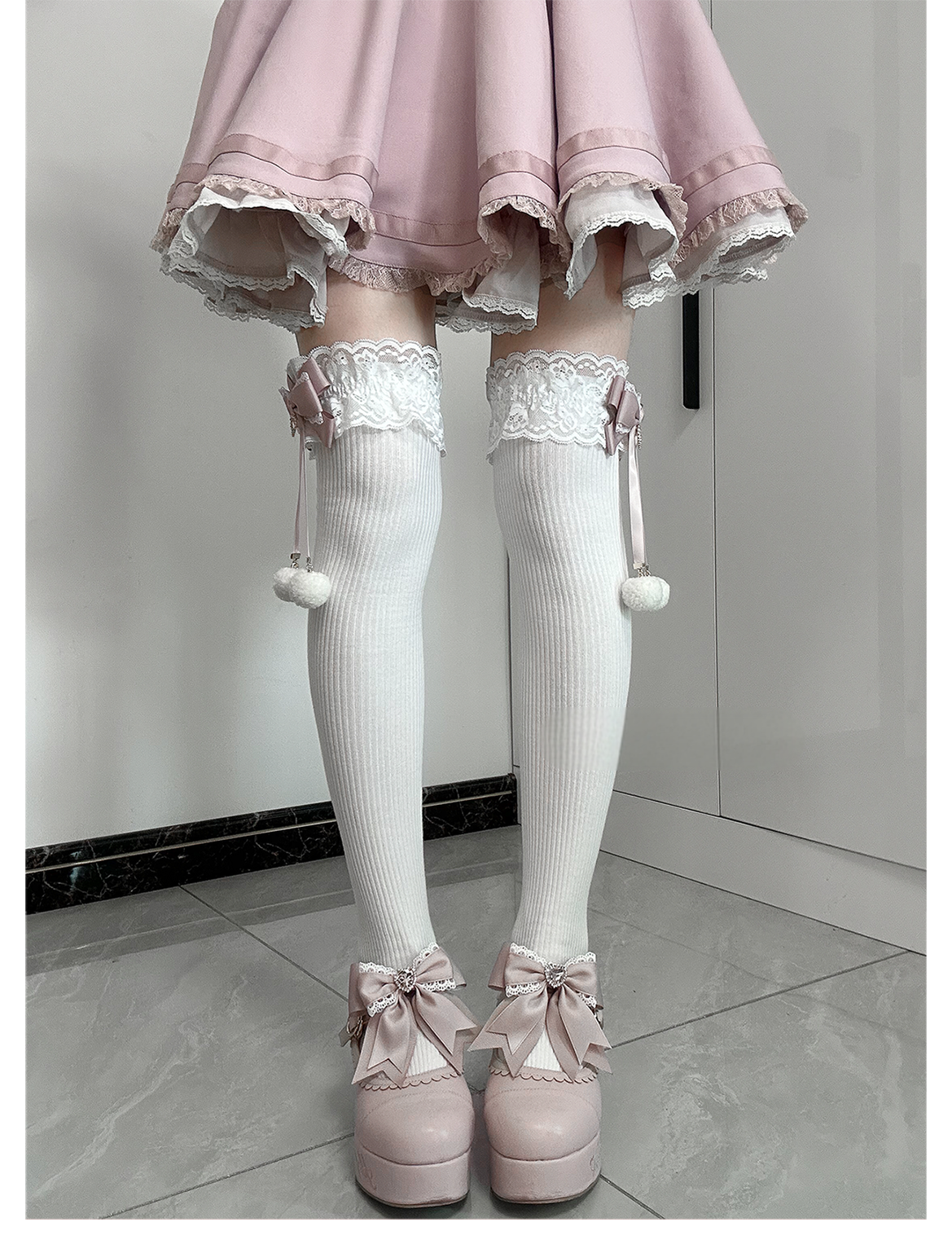 Jirai Kei black-pink knee-high socks on model full leg view showing sock height lace cuff detail pink bow and white pom-pom accent with platform styling