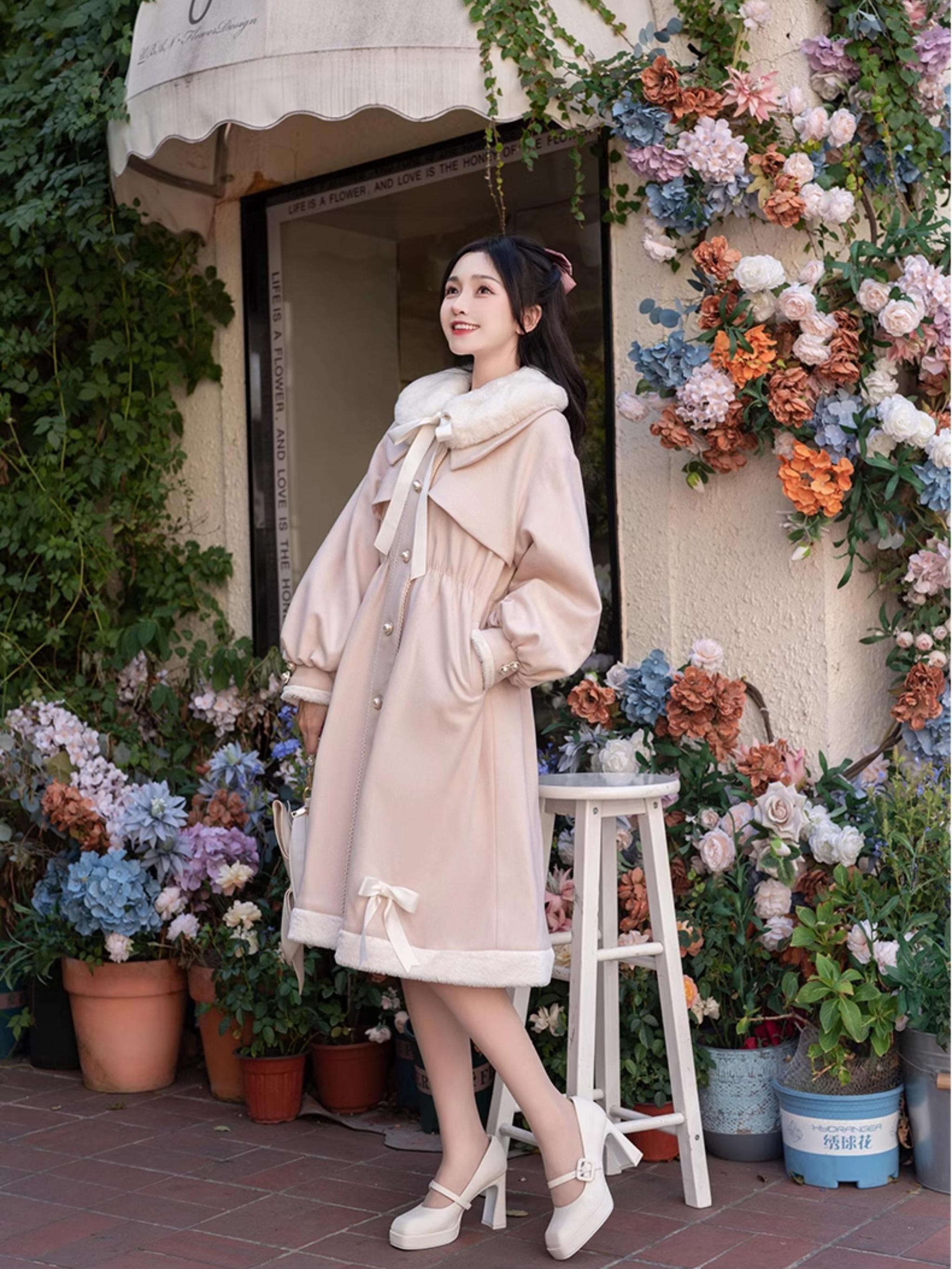 Light pink Ryousangata Jirai Kei winter coat side view - female model leaning on white stool wearing pink coat with button front, side pockets, and hem bow decorations