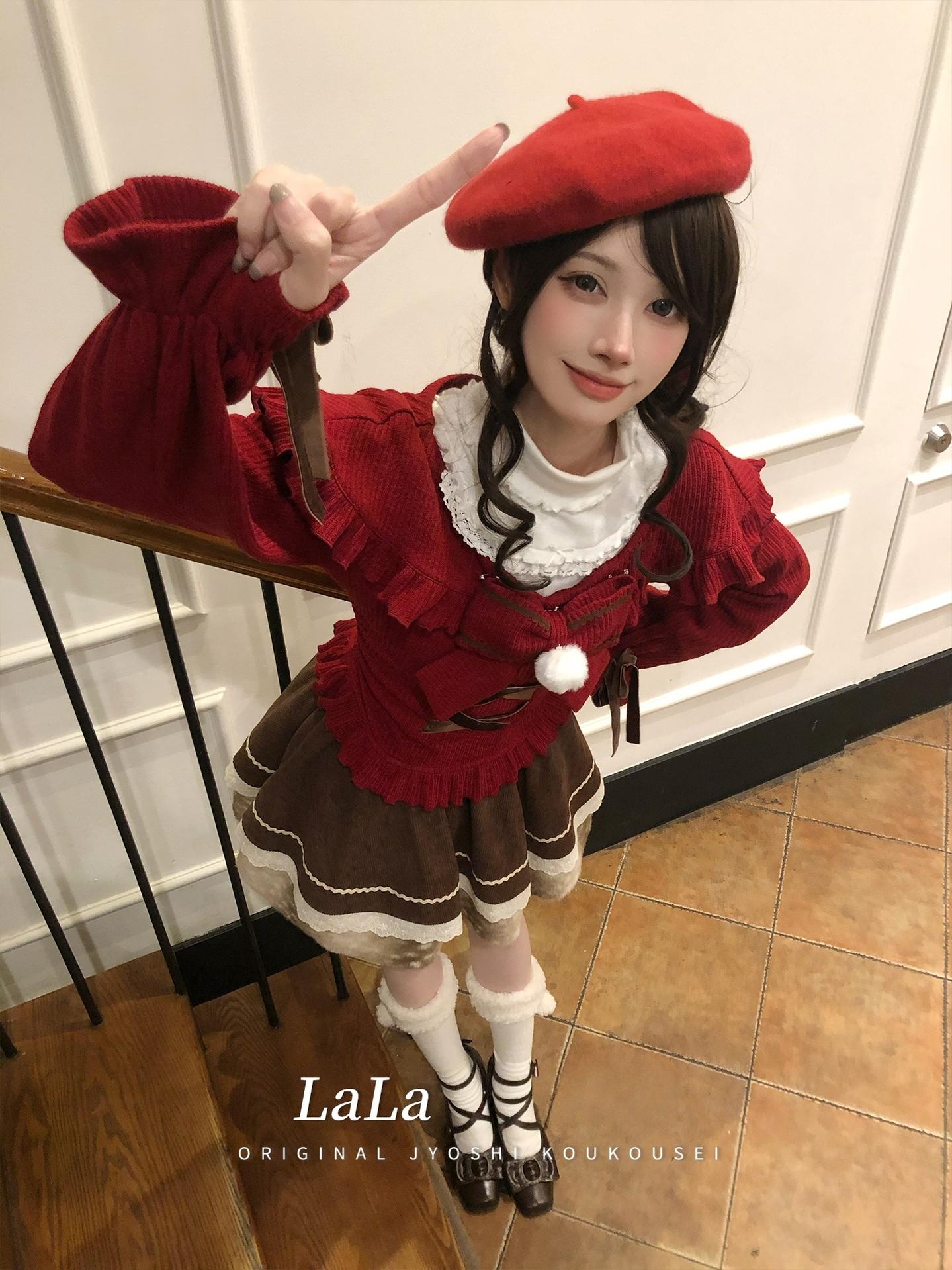Model posing on stairwell wearing red jirai kei sweater with cross-lace details and brown tiered skirt, demonstrating alternative fashion styling