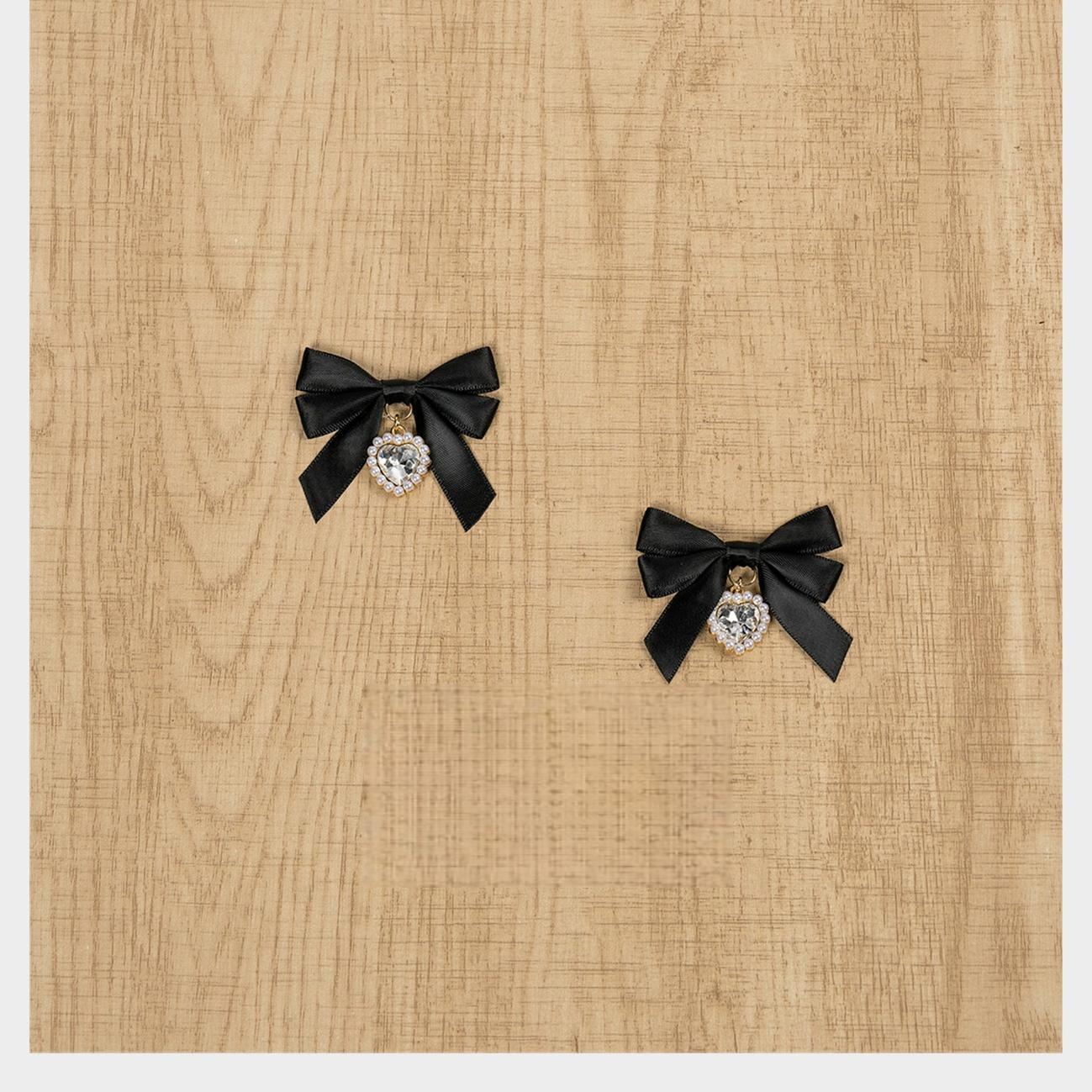Black satin Jirai Kei bow hair clips with round rhinestone pendant charms flatlay on natural wooden tabletop surface