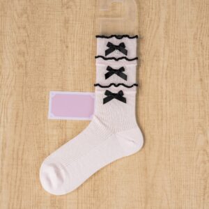 Light pink frilled mid-calf Jirai Kei socks with black satin bows and ruffled texture flat lay view on wooden surface
