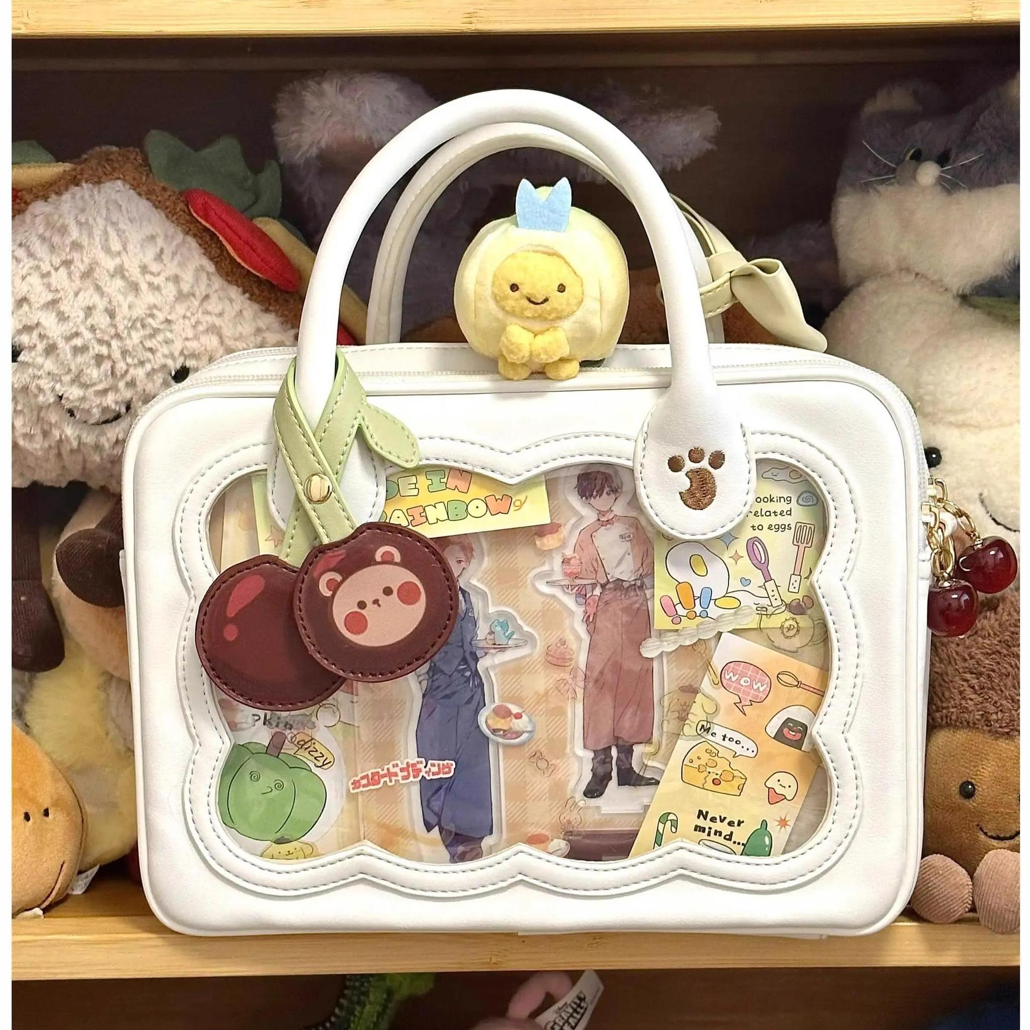 White cherry bear cookie Jirai Kei ita bag with clear window filled with anime goods and crown plush charm on handle indoor display