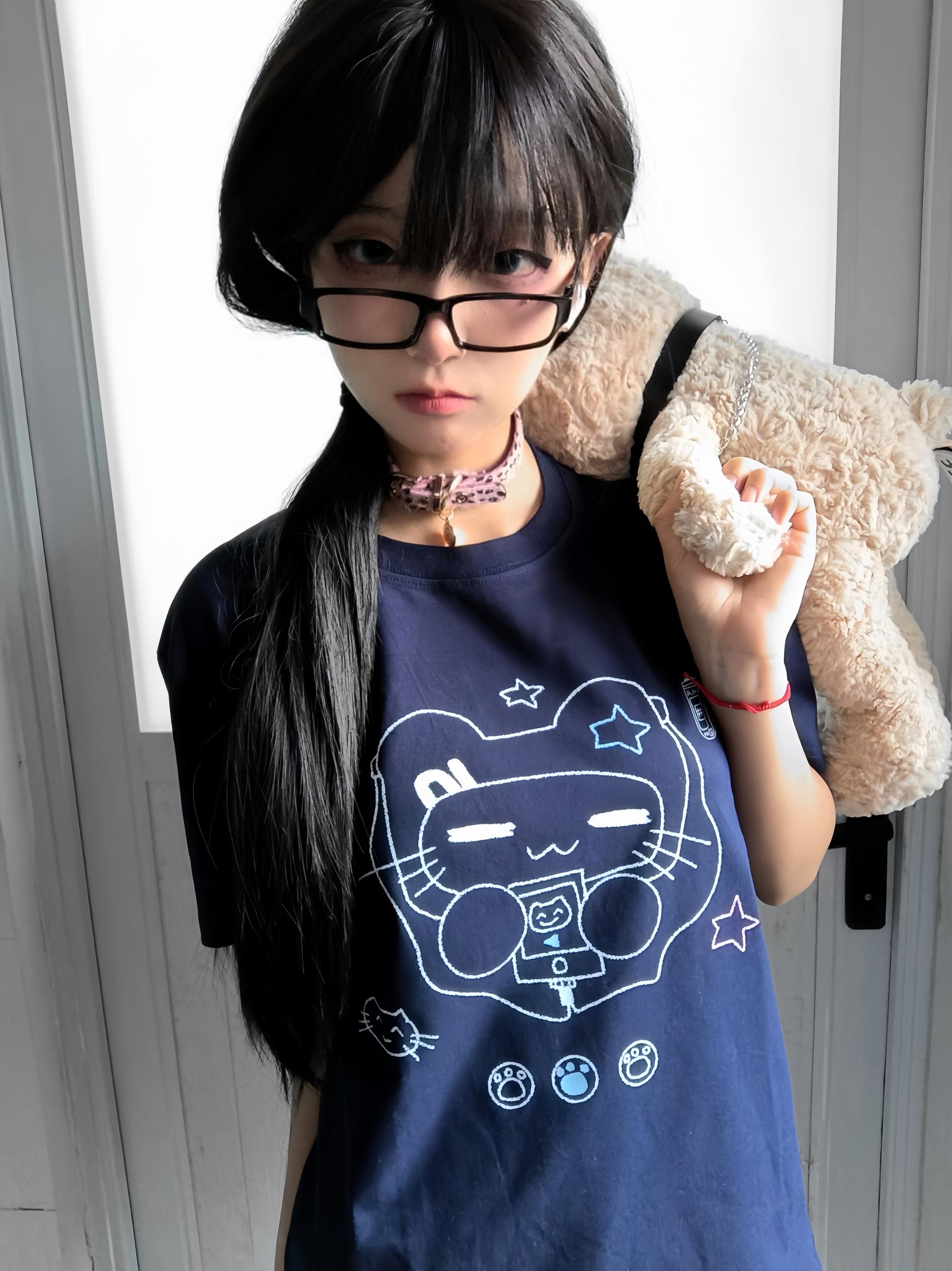 Model adjusting eyeglasses while wearing navy Jirai Kei cat headset graphic T-shirt with pink choker in white interior room