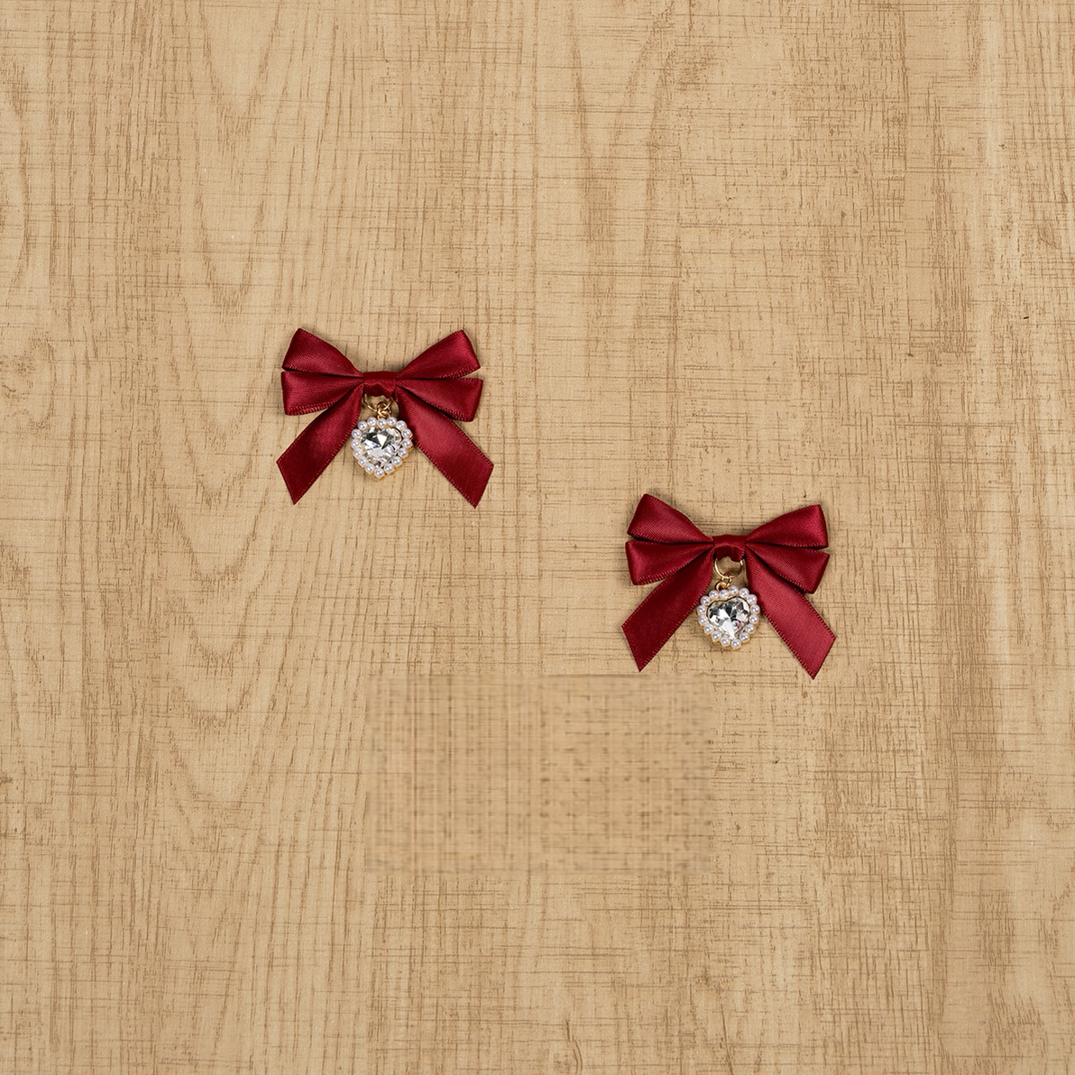 Red satin Jirai Kei bow hair clips with lustrous round rhinestone pendant charms displayed on natural wooden tabletop