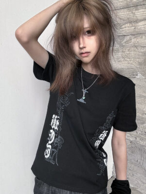 Black gothic cross printed jirai kei t-shirt front view on model with light brown hair and wooden wall background showcasing chest print and side torso graphics