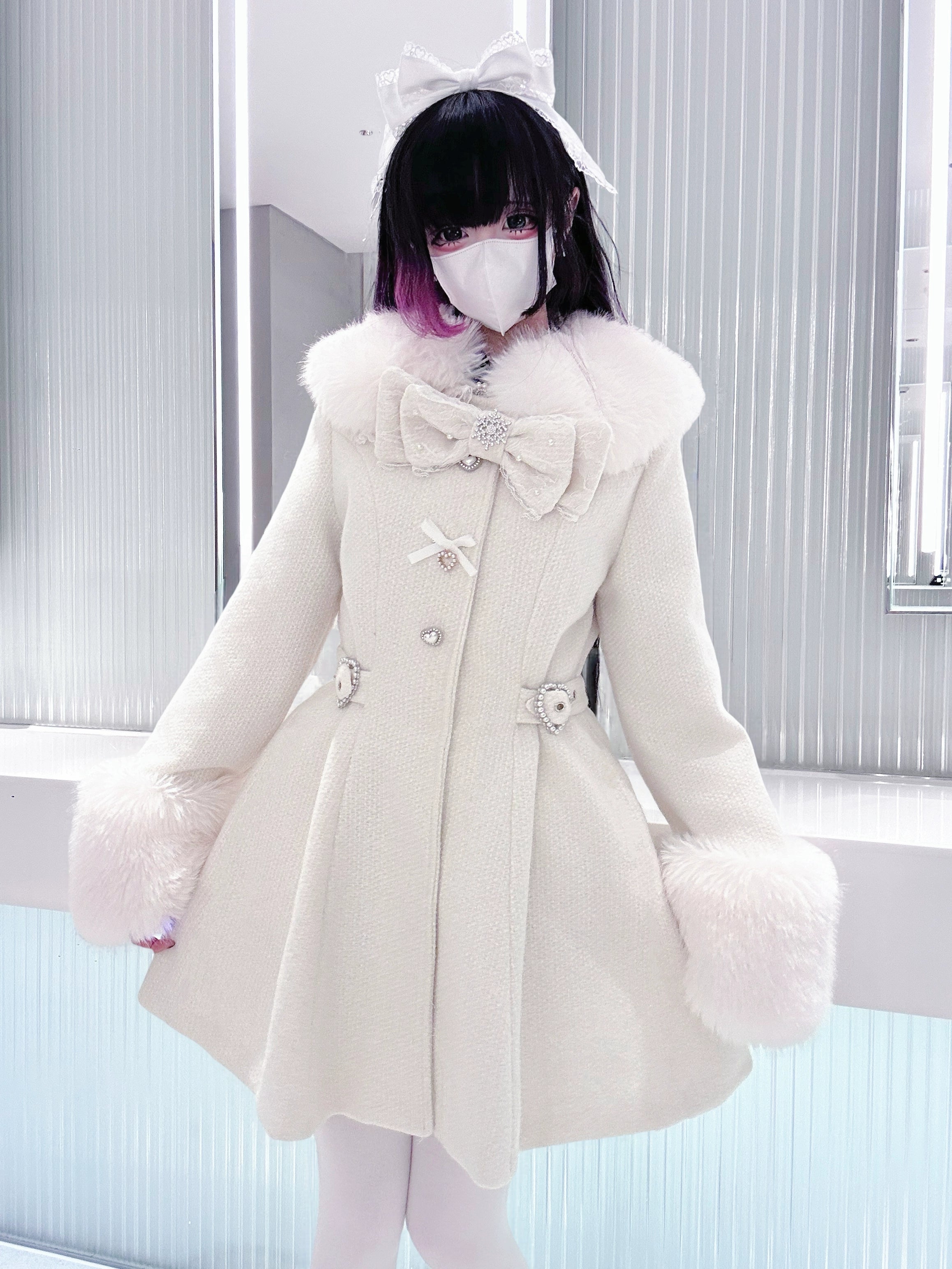 Beige Ryousangata winter coat three-quarter angle showing bow collar detail faux fur cuffs tailored waist shape modeled with gradient hair striped background