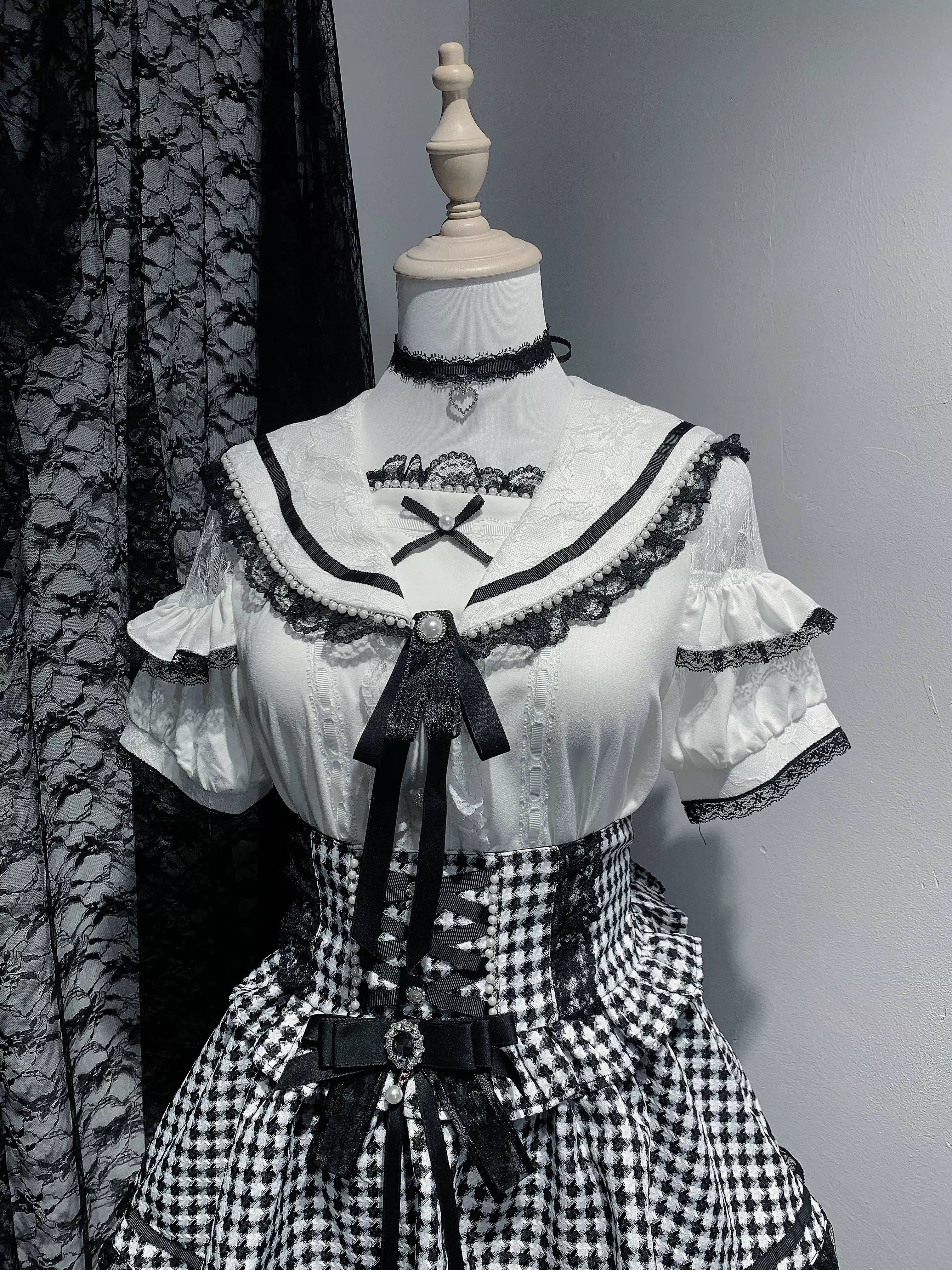 Short-sleeved white Jirai Kei sailor collar blouse with lace trim details, removable front bow, and decorative pearl buttons in studio presentation highlighting shoulder cutouts and refined craftsmanship