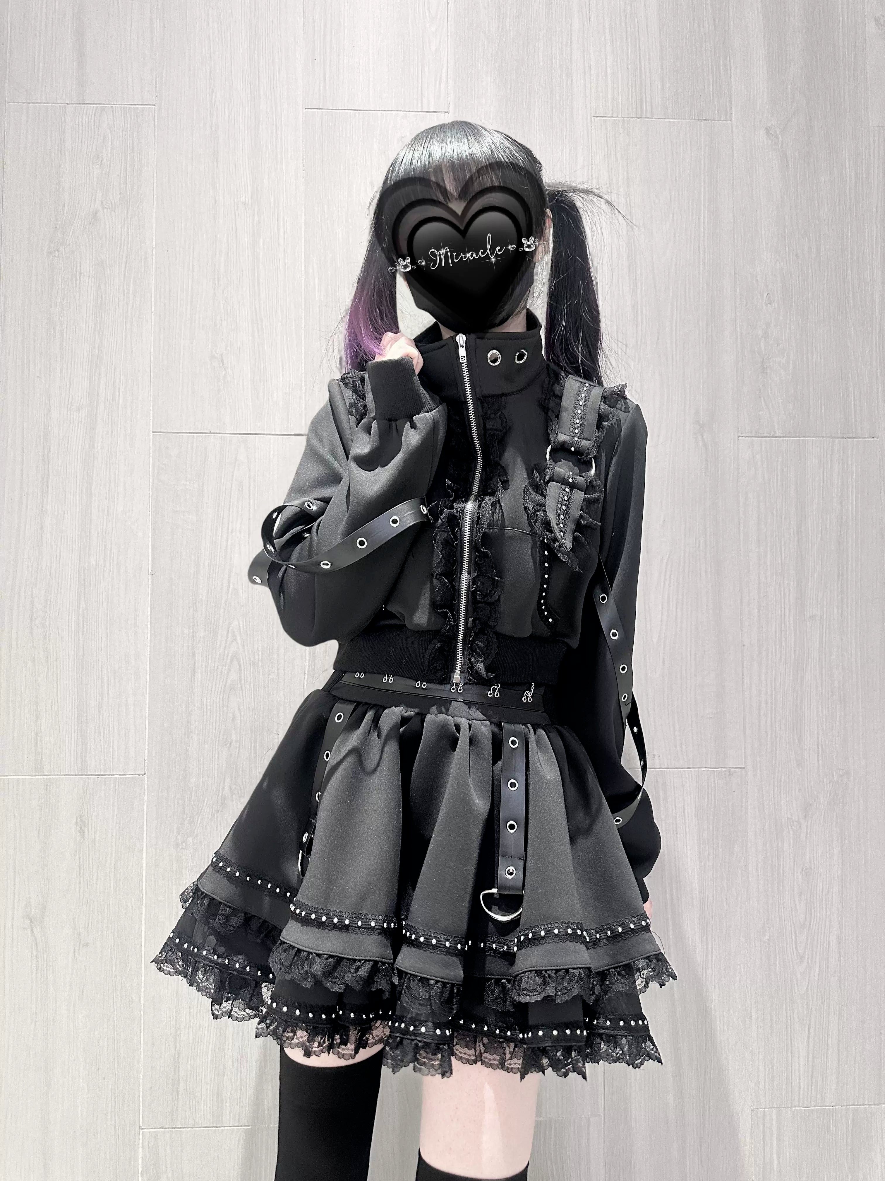 Gothic punk two-piece suit with cross zipper front buckle belt rivet trims lace hem skirt front three-quarter view wooden background