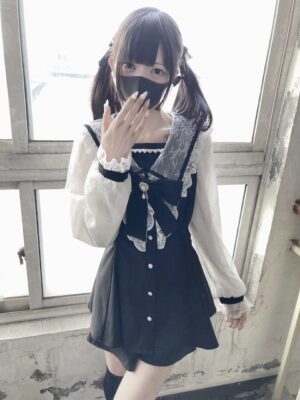 Side-front angle of black Jirai Kei dress featuring sheer lace sleeves, gem-decorated bow detail, composite sailor collar, and ruffled cuffs