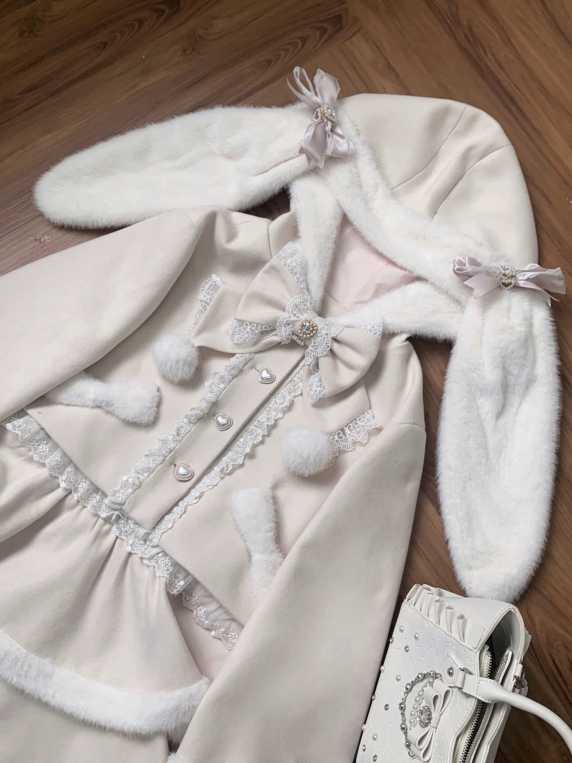Ryousangata Jirai Kei coat flat lay detail shot showing beige fabric, white fluffy fur trim, heart-shaped buttons, removable bow, lace and pom-pom decorations with matching studded handbag
