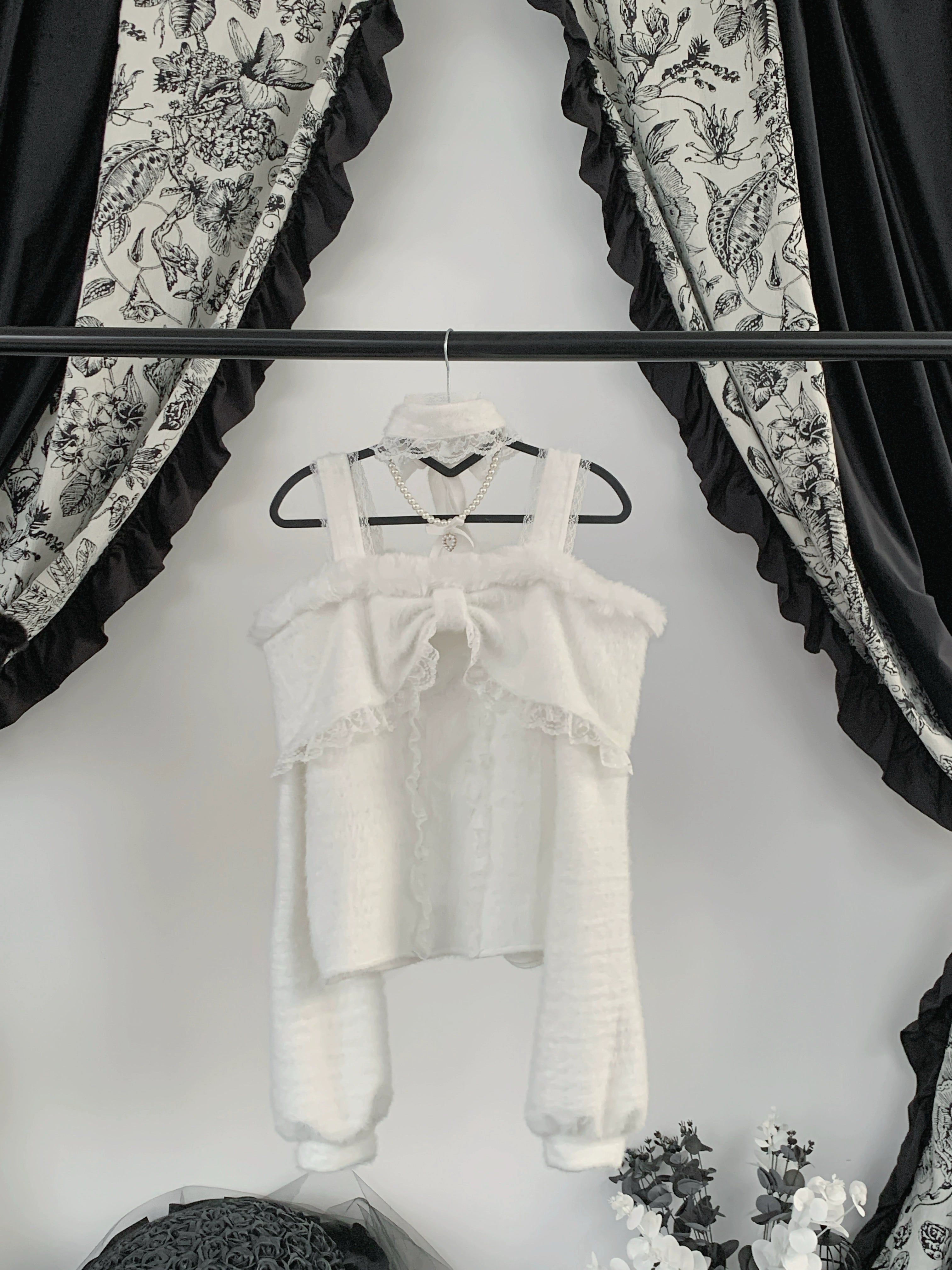 White off-shoulder cropped plush top hanging on display featuring front bow knot, crisscross back straps, and delicate lace trim details
