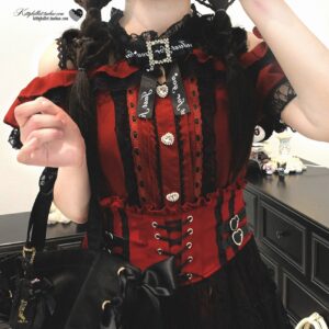 Red off-shoulder Jirai Kei blouse close-up detail shot showing black lace trim black lace trim corset-style lacing and rhinestone-embellished ribbon bow at vanity