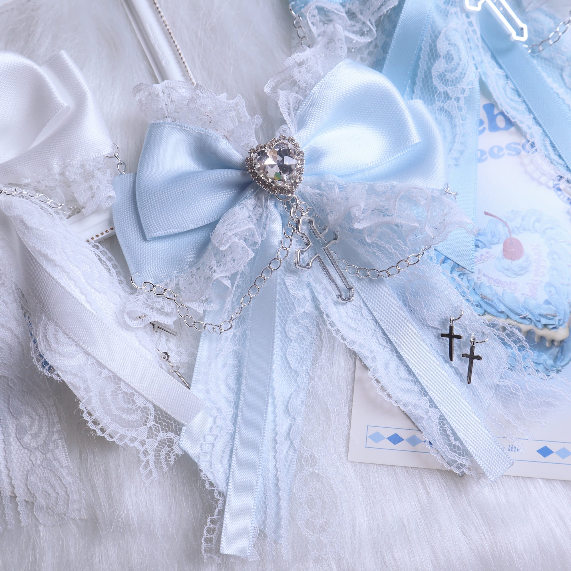 Baby blue satin bow hair clip flat lay close-up on fuzzy fabric with lace trim, heart-shaped rhinestone and silver cross charm decoration